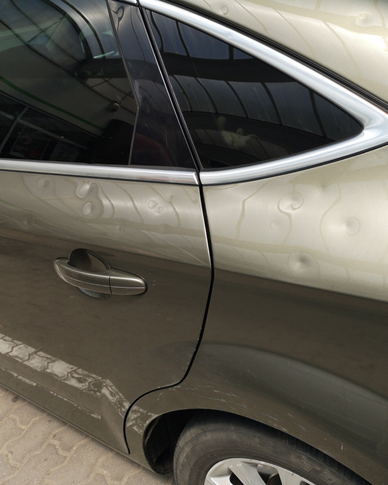 Wind-driven hail dents across a rear door and quarter panel of a bronze sedan in Arvada, CO