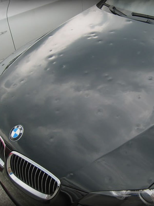 Close-up of hail dents across a dark vehicle hood photographed for a claim record