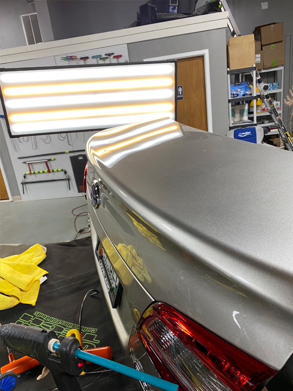 Silver trunk lid hail damage read under PDR reflection lighting at our Thornton, CO area hail repair shop